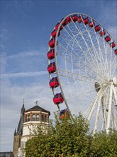 Red Ferris wheel next to a church tower and a historic building under a blue sky, Ferris wheel with