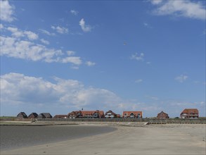 A sandy beach in front of a settlement with red houses, under a blue sky with white clouds, Baltrum