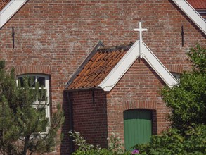 View of a brick church building with green painted door and white cross above, Baltrum Germany