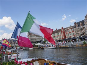 Flags waving on the banks of a river, people and historic buildings in the background, skyline of a