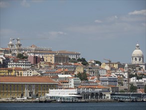 View of a city with various buildings, domes and red roofs by the water, Lisbon, Portugal, Europe