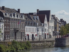 Rows of old town houses along the river with a flag and walkers, Maastricht, Netherlands