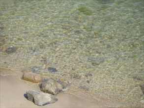 Clear water on the coastal shore with various stones on the sandy beach, spring on the Baltic Sea