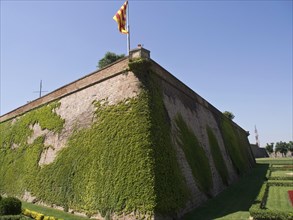 A fortress with high walls covered with climbing plants and a flag on top, barcelona, spain