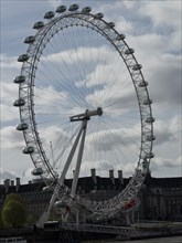 A large Ferris wheel stands majestically against a cloudy sky in an urban landscape, London,