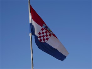 The Croatian flag fluttering in the wind against a clear blue sky, with its characteristic red and