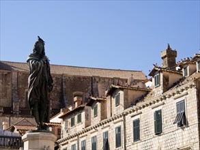 Statue in front of historic buildings with tiled roofs under a bright blue sky, the old town of