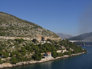 Coastal landscape with mountains, hills, bridges and houses on the shore of the calm blue sea under