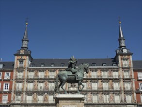Historic square with central equestrian statue in front of a detailed building with towers under a
