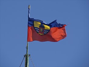 A flag with a coat of arms fluttering vividly in the wind against a clear blue sky, Borkum,