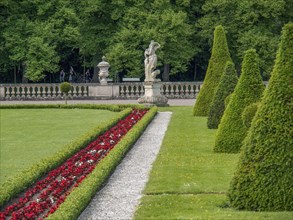 Flower beds and well-kept garden with a statue and a historic castle in the background under a