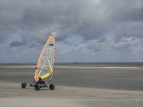 Person driving a kite buggy along the beach, in the background the sea under a cloudy sky,