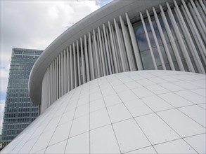 White, curved structure in front of a modern glass facade under a cloudy sky, modern buildings with