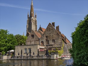 A large old brick church building with green plants and boats by the river under a blue sky,