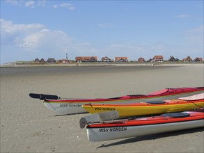Several kayaks on the beach with a view of a coastal landscape and traditional houses, Baltrum
