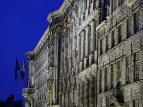 Richly decorated illuminated facade of a historic building against a deep blue sky at night, blue