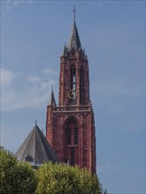 A gothic tower in red colour rises in a clear blue sky, part of a historic church, Maastricht,