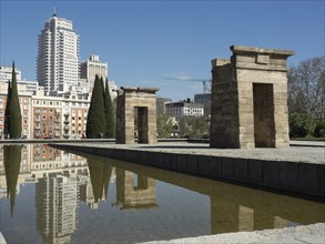 Two ancient temple pylons reflected in the water with modern skyscrapers in the background under a