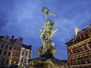 A square by night with a statue and illuminated buildings with flags, the historic market square of