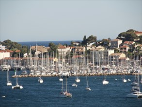 Overview of a marina with many sailing boats lying in front of a coastal town and a blue sky, la
