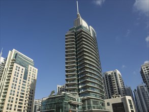 A modern high-rise building with a glass facade in an urban setting under a blue sky, dubai, arab