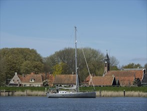 A sailing boat in front of a village with traditional houses and trees on the shore, Enkhuizen,