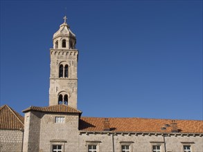 Church with bell tower in front of a bright blue sky, in the foreground buildings with red roofs,