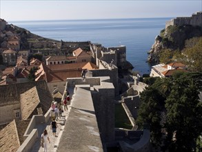 People walking on a city wall with a view of the city and the sea, the old town of Dubrovnik with