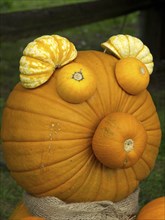 A large orange pumpkin with smaller pumpkins as ears and nose, decorated like a face, many