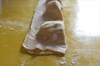 Preparation of fresh homemade pasta mezzaluna with ricotta, folded dough in front of cutting out