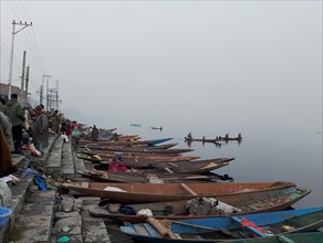 Foggy lakeside with docked wooden boats and people in a calm, misty morning atmosphere