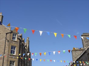Colourful flags hang over an old town with buildings and windows under a blue sky, the atmosphere