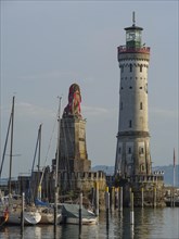 Lighthouse and lion sculpture at the harbour in late afternoon light with boats, towers at a