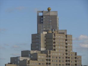 A modern, tall building with a golden ornament at the top under a clear blue sky with few clouds,