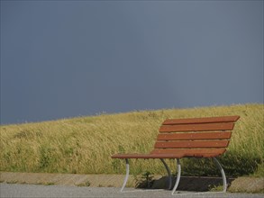 Lonely wooden bench on a grassy field under a dark, cloudy sky, Baltrum Germany