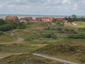 View of houses in the dunes with green vegetation and sea in the background under a cloudy sky,