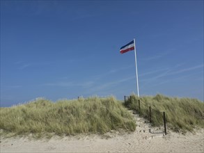 Sand dunes with stairs and flag on a sunny day under blue sky, Heligoland, Germany, Europe