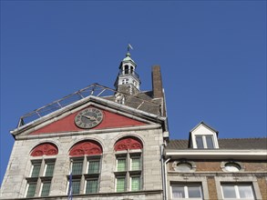 Historic town hall building with bell tower and clock face under a bright blue sky, Maastricht,
