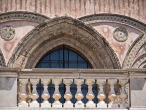 An arched window with ornate stone ornaments on a historic pink building, palermo in sicily with an