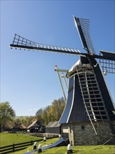 Majestic windmill against a clear blue sky, with surrounding trees and buildings in spring,