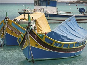 Two blue and yellow Maltese boats in the harbour, the water is calm and turquoise, colourful boats