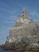 A historic stone church perched on rocky cliffs on the coast against a clear sky, Bari, Italy,