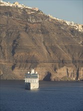 A cruise ship sails along the sea, past steep cliffs in Santorini, The volcanic island of Santorini