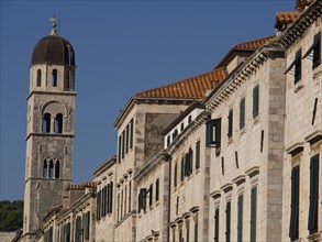 Bell tower and buildings with stone walls and shutters under a blue sky, the old town of Dubrovnik