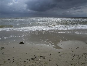 Restless waves on a sandy beach under a cloudy sky. The sea looks impetuous and agitated, view of