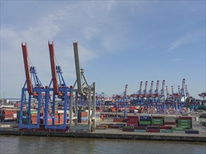An industrial harbour terminal with lots of containers, cranes and storage areas on a sunny day, a