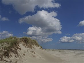Sand dunes on a beach with a bright blue sky and white clouds above, Baltrum Germany