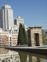 Ancient temple next to modern skyscrapers with reflections in the water under a clear sky, Madrid,