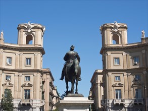 Symmetrical buildings with an equestrian statue of a historical figure in the centre, under a blue