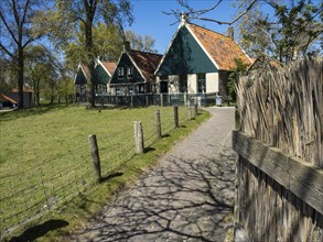A cobbled path leads past traditional green houses and fences in a rural setting, Enkhuizen,